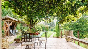 Un patio con tavolo e sedie, immerso nel verde e circondato da una recinzione in legno.