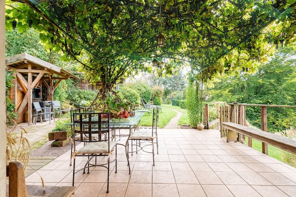 Une terrasse avec une table et des chaises, entourée de verdure et d’une clôture en bois.