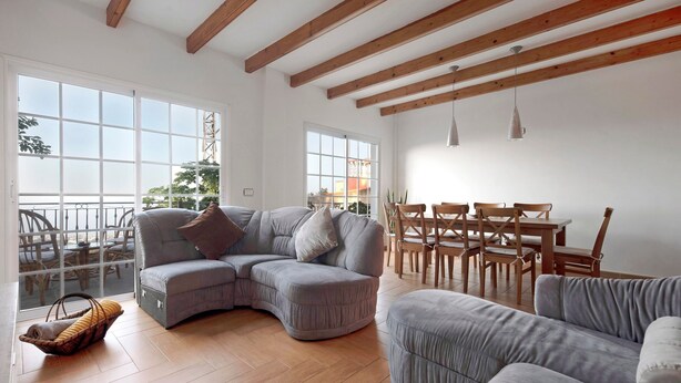 A spacious living room with a large L-shaped grey sofa, a dining area with wooden chairs and a table, and large windows allowing natural light. - Pet-Friendly Vacation Home "Casa Luz" with Sea View, Whirlpool & Wi-Fi (La Luz)