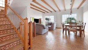 A spacious living area with a wooden staircase, a dining table with chairs, and a large window providing natural light. - Pet-Friendly Vacation Home "Casa Luz" with Sea View, Whirlpool & Wi-Fi (La Luz)