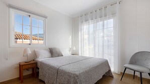 A bedroom with a bed, a nightstand, a chair, a window with a view, and sheer curtains. - Pet-Friendly Vacation Home "Casa Luz" with Sea View, Whirlpool & Wi-Fi (La Luz)