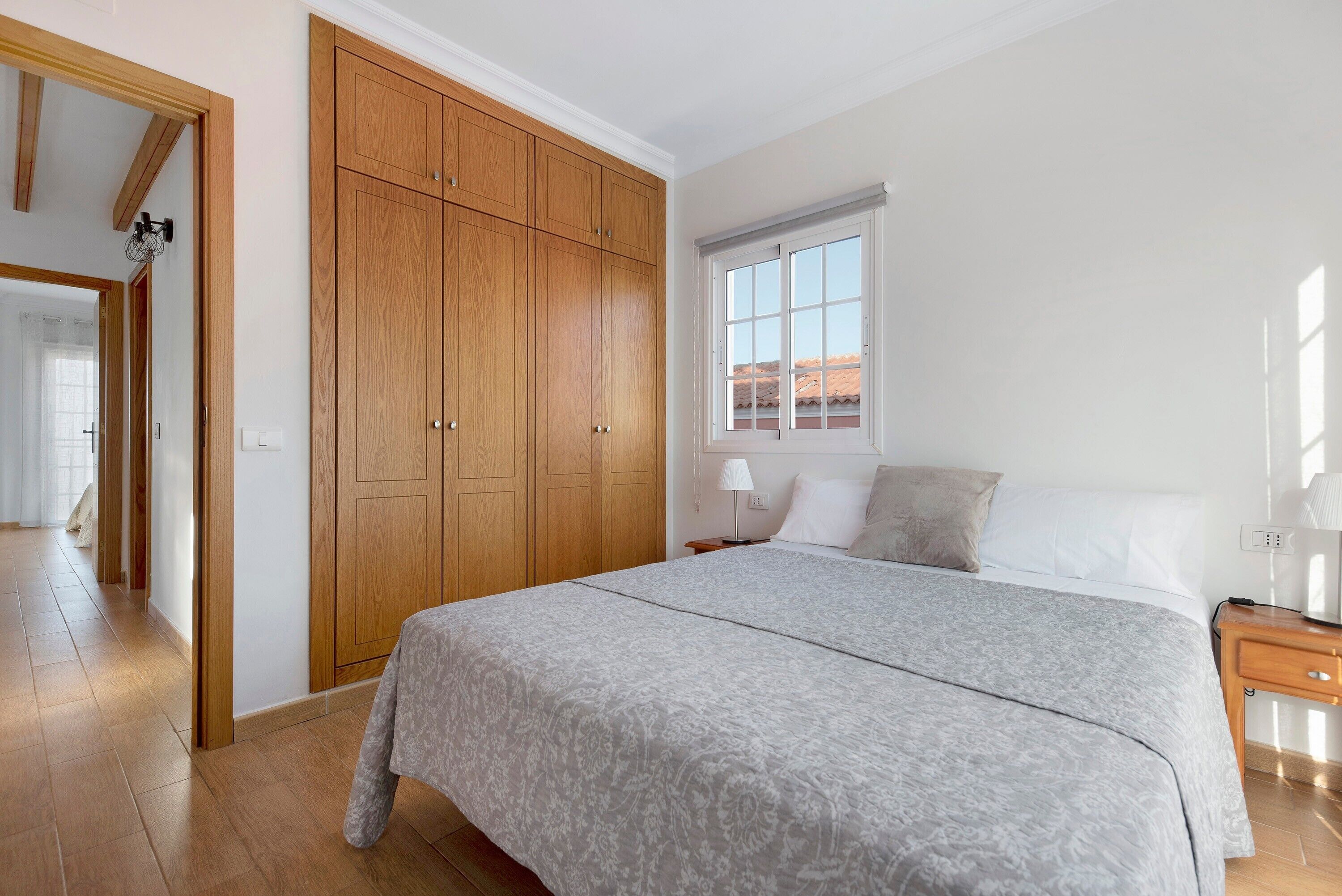 Un dormitorio con una cama grande, un armario de madera, una ventana y una mesita de noche.