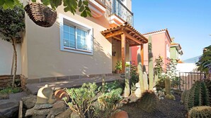 A building with a balcony, a window, and a garden with cacti and rocks. - Pet-Friendly Vacation Home "Casa Luz" with Sea View, Whirlpool & Wi-Fi (La Luz)