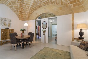Une salle à manger avec un plafond en pierre, une table ronde et des chaises. On y trouve un lustre et un miroir au mur.