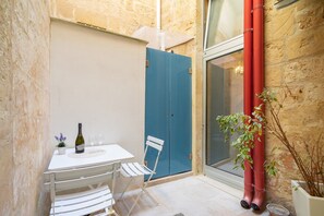 Un petit espace extérieur aménagé avec une table, des chaises, une bouteille de vin et une plante en pot.
