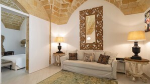 Una sala de estar acogedora con un sofá blanco, dos mesitas de noche con lámparas, un espejo decorativo y una alfombra verde.