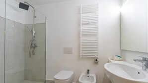 Un baño moderno con ducha acristalada, inodoro, bidé y un lavamanos amplio.