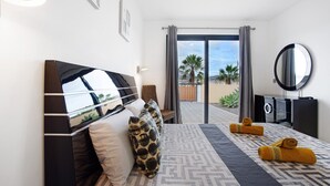 Une chambre d’hôtel moderne dotée d’un grand lit, d’un téléviseur à écran plat, d’un miroir et offrant une vue sur les palmiers.