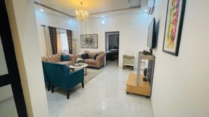 A spacious living room with a chandelier, a sofa set, a TV, and a painting on the wall.