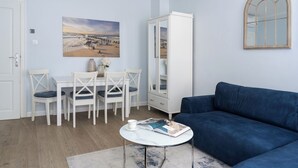 A living room with a blue sofa, a white cabinet, a dining table with chairs, and a painting on the wall. - Parkowa 33A2 - Beachfront Apartment with Parking by Lion Apartments Sopot (Sopot)