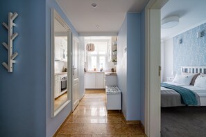A narrow hallway leading to a kitchen and a bedroom with a bed and a nightstand.
