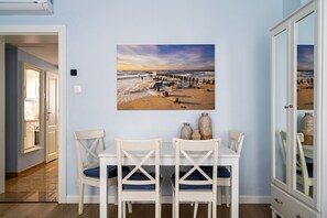 A dining area with a table and chairs, a painting of a beach scene, and a cabinet with glass doors.