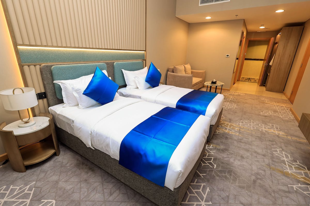 A hotel room with two beds, a nightstand, a lamp, and a seating area.