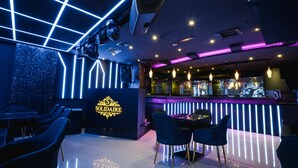 Zona de bar moderna con iluminación de neón, una barra y diferentes disposiciones de asientos.