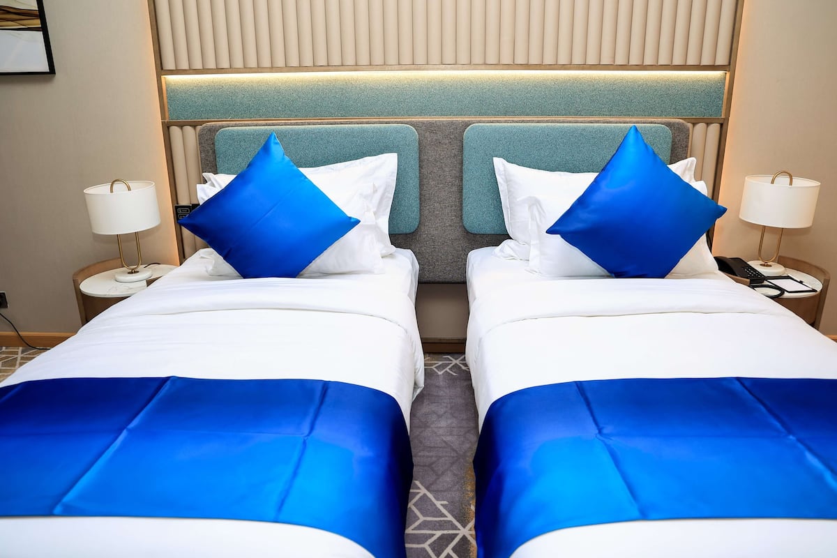 A hotel room with two beds, each with a blue bedspread and pillows, and a headboard with a textured design.