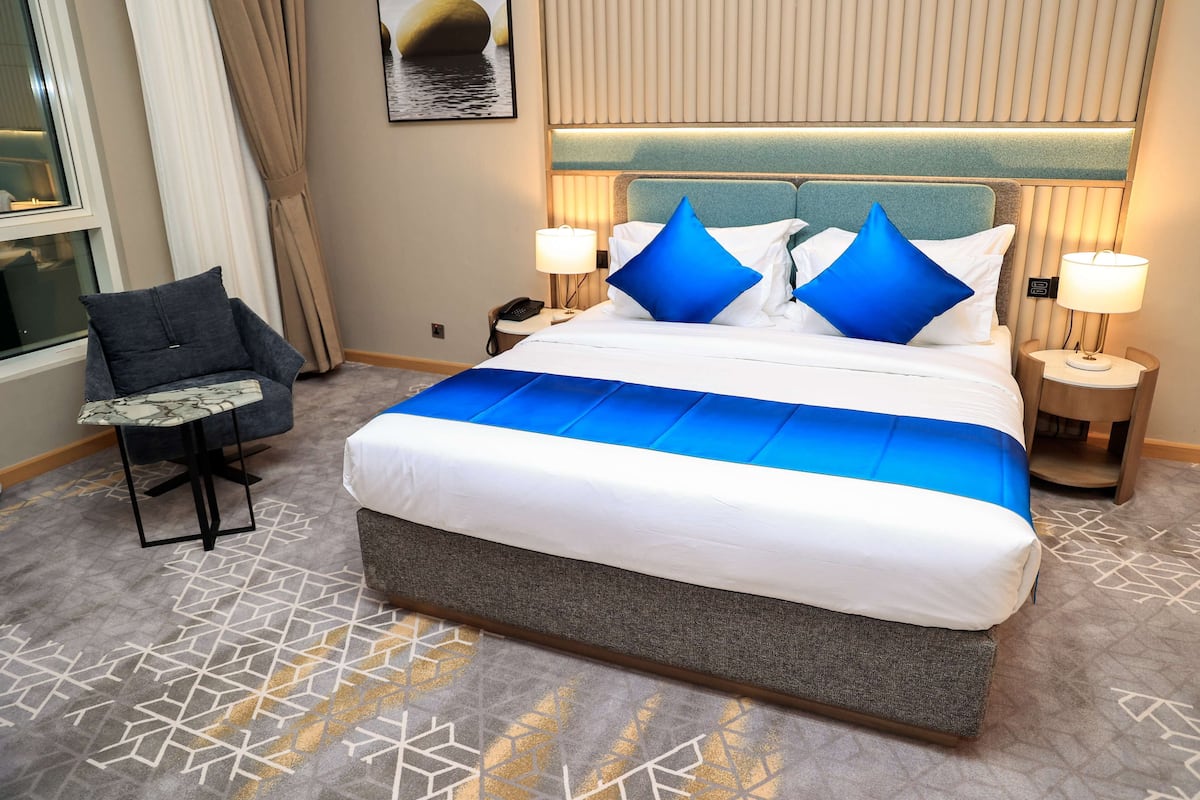 A hotel room with a large bed, two bedside tables with lamps, a chair, and a patterned carpet.