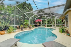A pool area with a glass enclosure, surrounded by potted plants and a red umbrella.