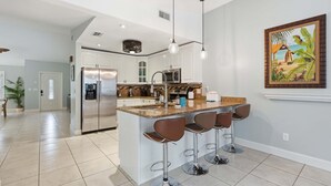 A modern kitchen with a central island, bar stools, stainless steel appliances, and pendant lighting. - Centrally Located Pool Home in Naples (Naples)