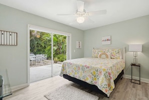 A bedroom with a bed, a ceiling fan, a window, and a door leading to a patio with outdoor furniture.