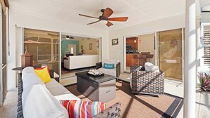 A spacious living area with a ceiling fan, a sofa with colorful cushions, a coffee table, and a wicker chair. - Centrally Located Pool Home in Naples (Naples)