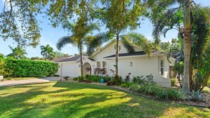A residential house with a well-maintained lawn, a variety of plants, and a clear sky. - Centrally Located Pool Home in Naples (Naples)