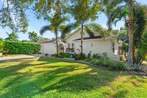 A residential house with a well-maintained lawn, a variety of plants, and a clear sky. - Centrally Located Pool Home in Naples (Naples)