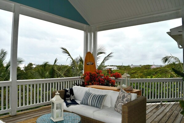 A covered outdoor seating area with a white cushioned sofa, a surfboard, and a lantern.