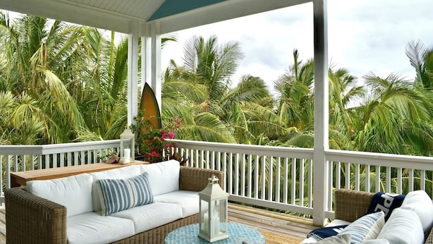 A covered porch with a white railing, wicker furniture, and a view of palm trees. - Kokomo Cay - Luxurious Home Near the Beach, with Spectacular Ocean Views (Hope Town)