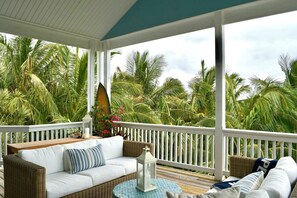 A covered porch with a white railing, wicker furniture, and a view of palm trees. - Kokomo Cay - Luxurious Home Near the Beach, with Spectacular Ocean Views (Hope Town)