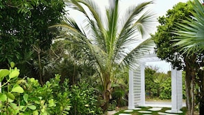 A garden with a white pergola, lush greenery, and a stone pathway. - Kokomo Cay - Luxurious Home Near the Beach, with Spectacular Ocean Views (Hope Town)