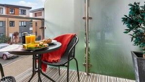 A balcony with a table set for breakfast, a chair, a potted plant, and a view of the street and buildings. - Stones Throw by Interhome (Charlestown)