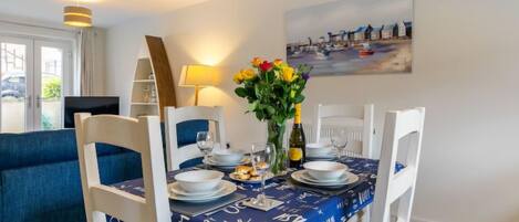 A dining area with a table set for four, a vase of flowers, and a painting on the wall.