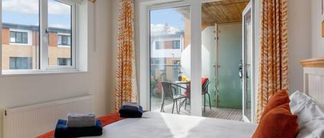 A hotel room with a bed, a radiator, a window, and a view of the outside.