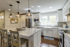 A modern kitchen with white cabinets, stainless steel appliances, and pendant lighting.