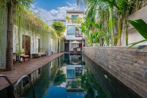 Uma área de piscina interior tranquila, com vista despejada para o céu, rodeada por vegetação exuberante e um edifício moderno com grandes janelas.