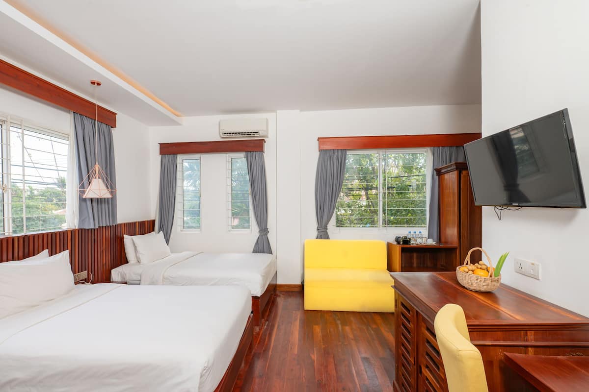 Une chambre d’hôtel avec deux lits, un canapé jaune, un bureau en bois, une télévision et de grandes fenêtres avec des rideaux.
