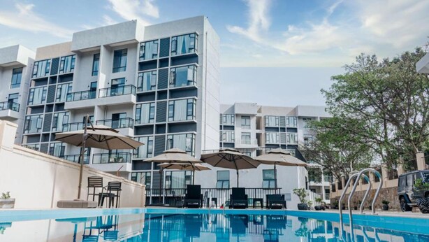 Un hotel moderno con piscina, mobiliario exterior y varios balcones.