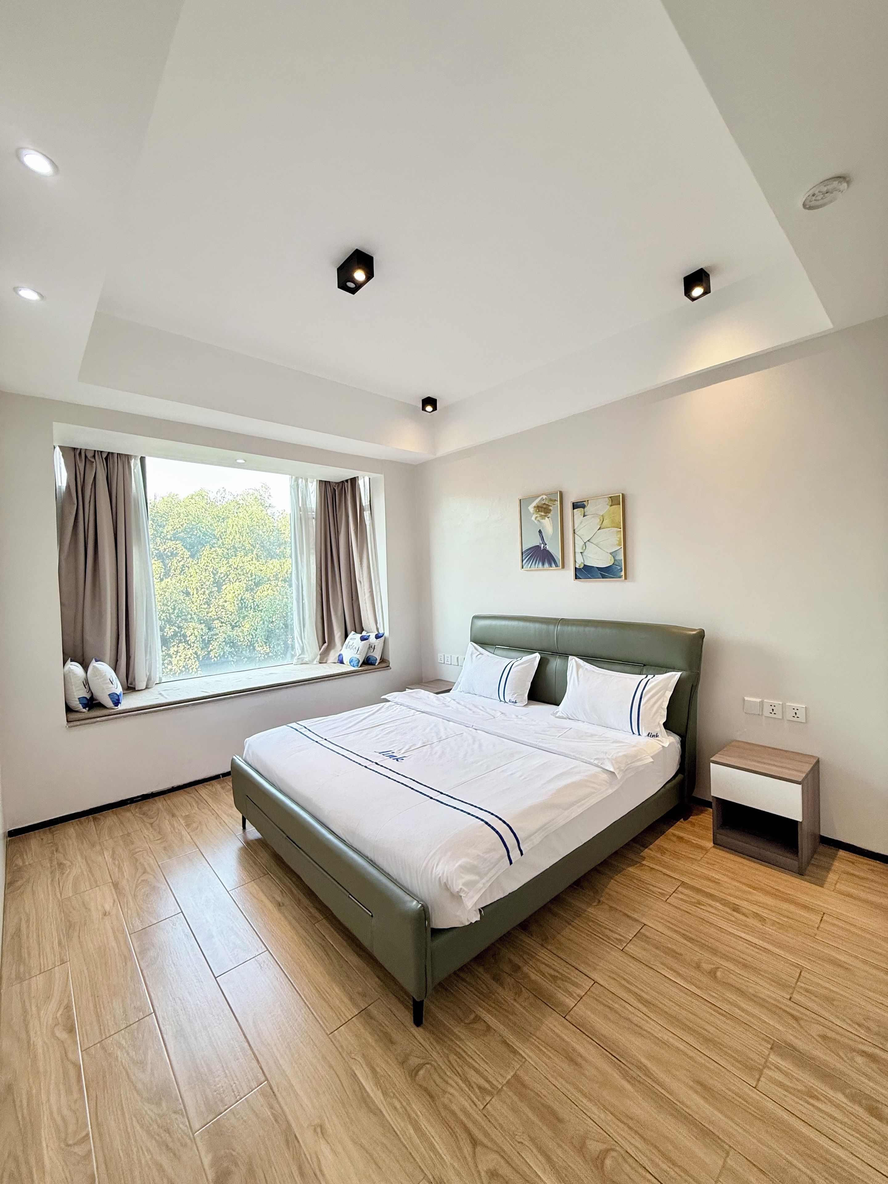 A modern bedroom with a large bed, a window with curtains, and a nightstand.