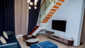 Una sala moderna con sofá, reposapiés, televisor y una escalera.