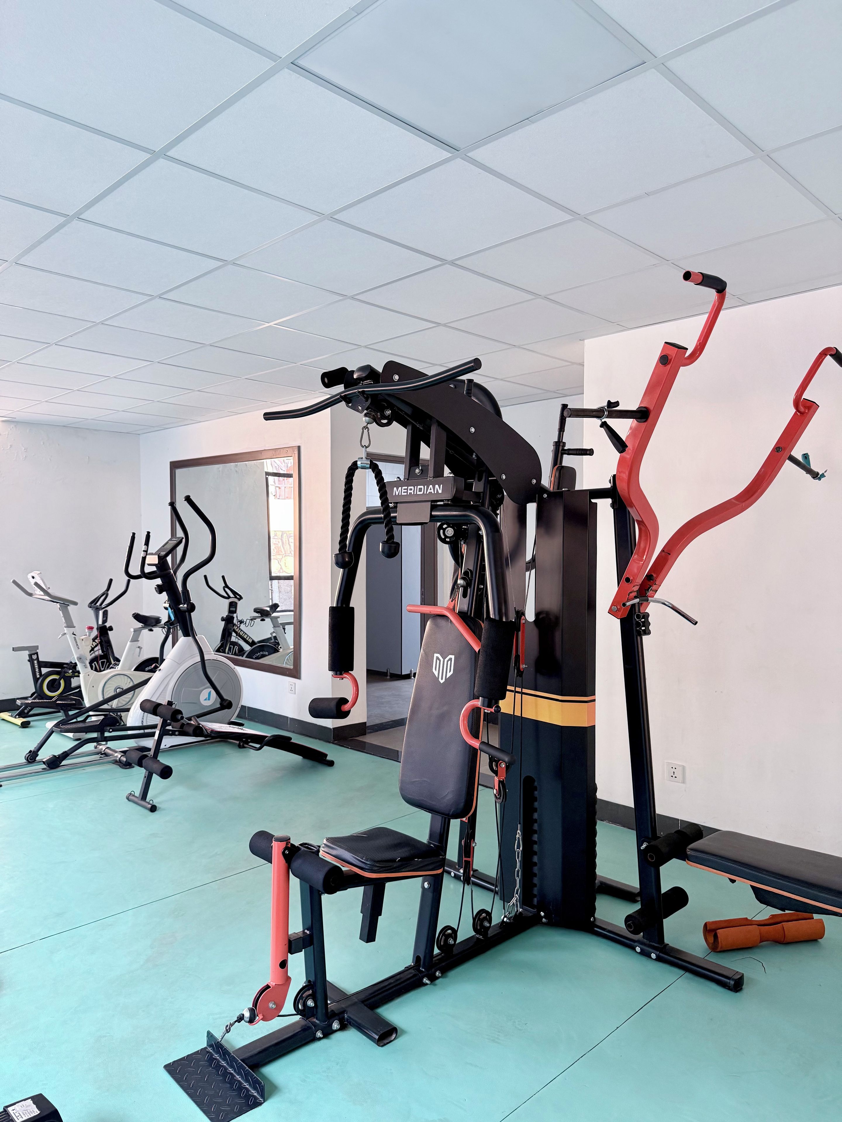 Un gimnasio con diversos equipos de ejercicio, incluyendo una máquina de remo, una bicicleta estática y una prensa de banca.
