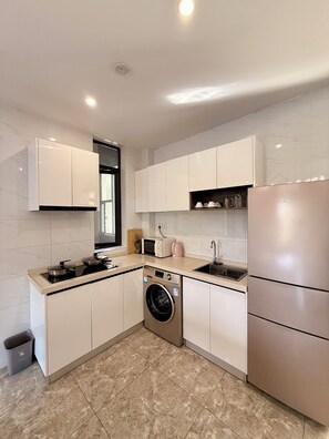 A modern kitchen with white cabinets, a stainless steel refrigerator, a built-in washing machine, and a microwave. - Elizabeth Golf Apartment (Kigali)