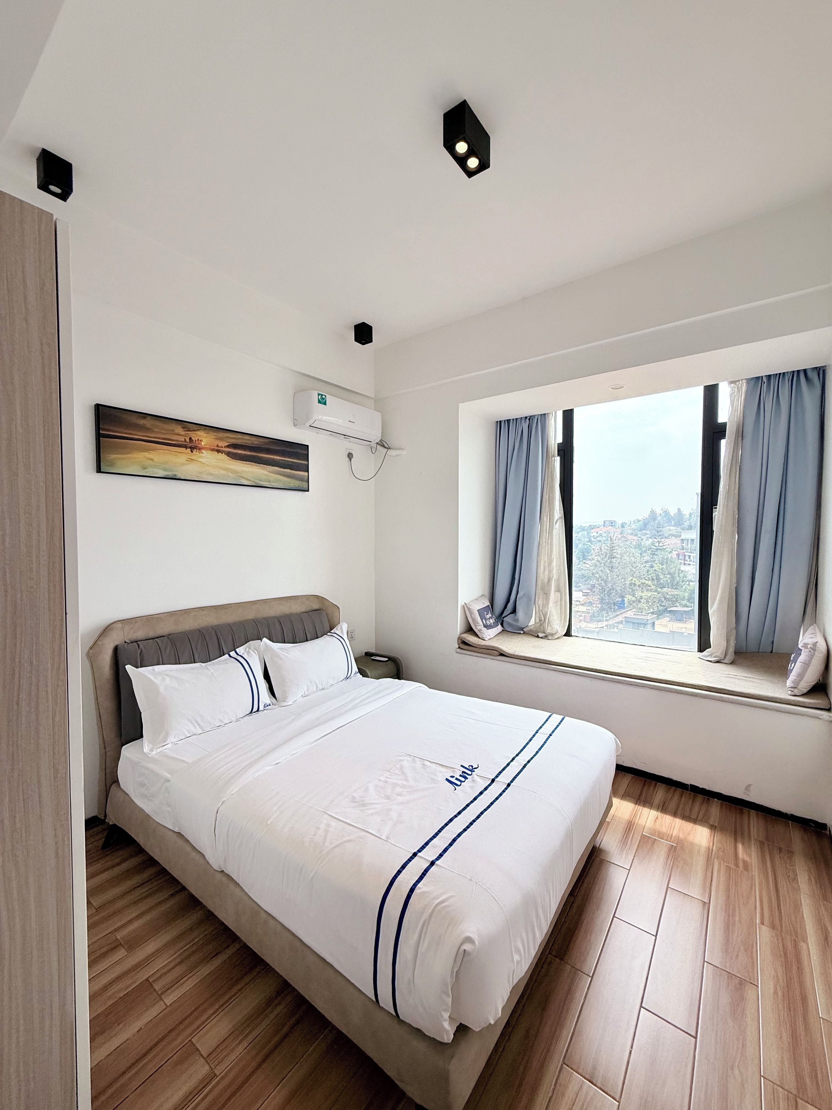 Habitación de hotel con cama, ventana con cortinas, un cuadro en la pared y un equipo de aire acondicionado.