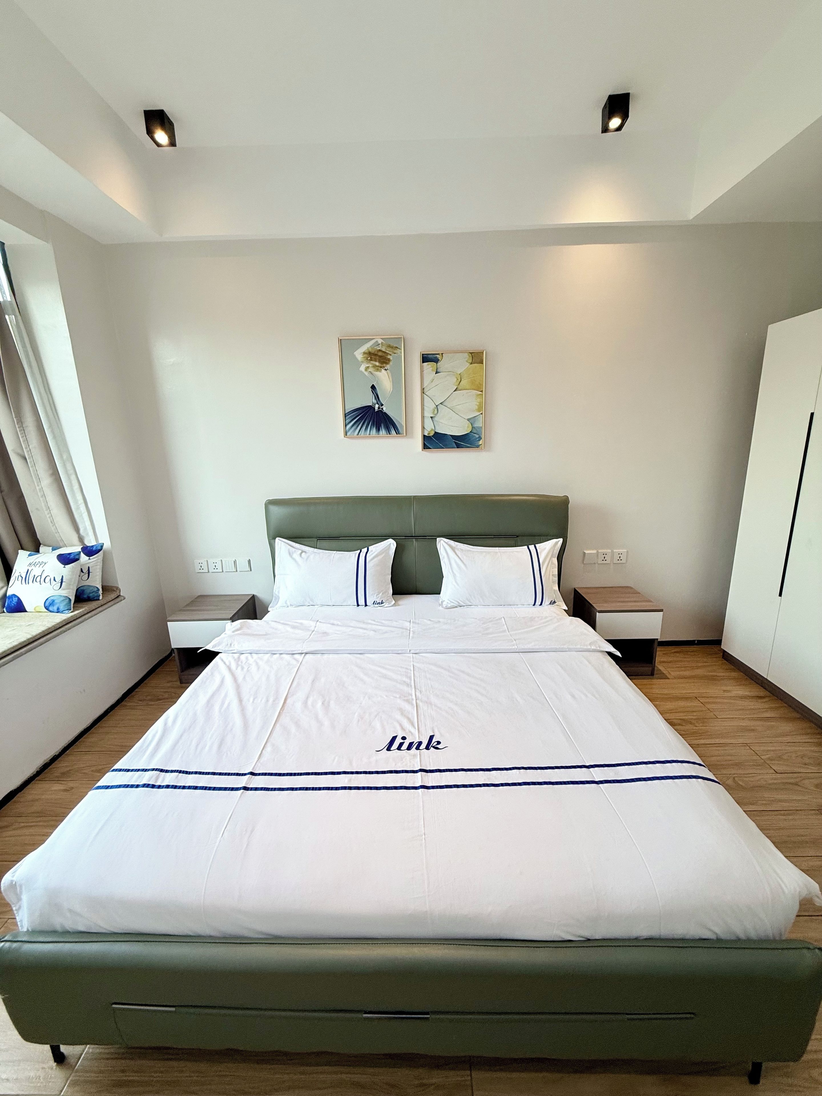 A hotel room with a large bed, a headboard, two wall-mounted artworks, bedside tables, and a wardrobe.