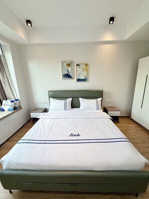 A hotel room with a large bed, a headboard, two wall-mounted artworks, bedside tables, and a wardrobe. - Elizabeth Golf Apartment (Kigali)