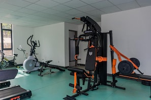 Un gimnasio con equipamiento de ejercicio, que incluye una banca, una máquina de pesas y una bicicleta estática.