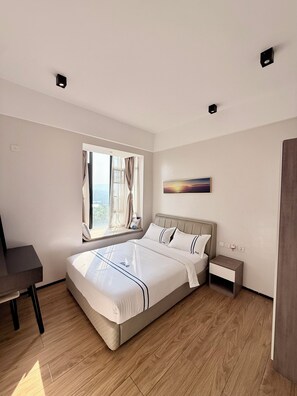 A modern hotel room with a large bed, a desk, and a window with curtains. - Elizabeth Golf Apartment (Kigali)