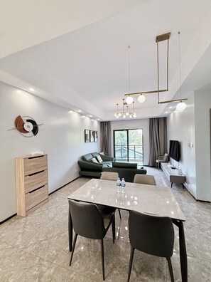 Una sala de estar moderna con comedor, sofá, televisor y mueble de madera.