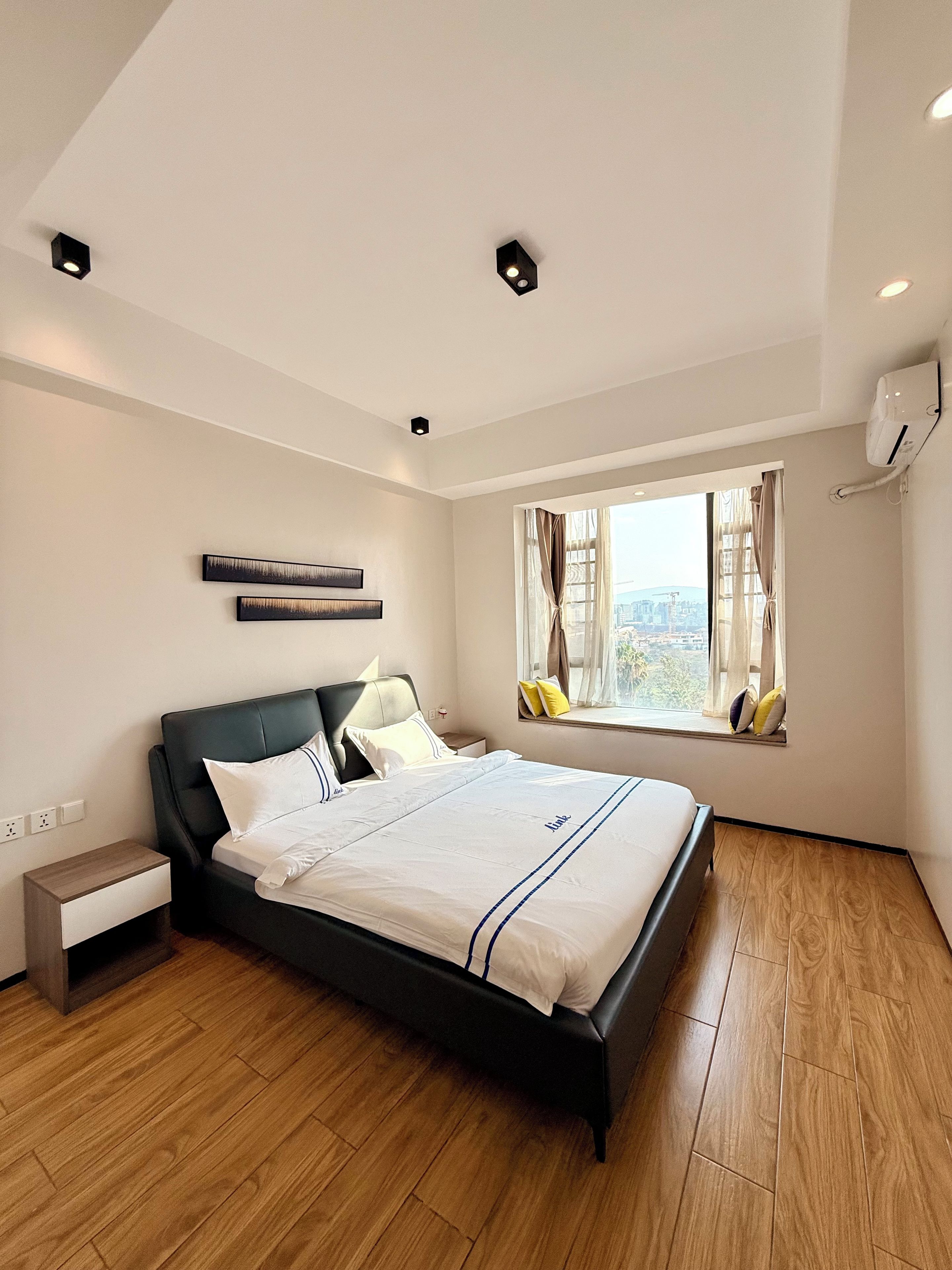 A modern hotel room with a large bed, a nightstand, a window with curtains, and a city view.