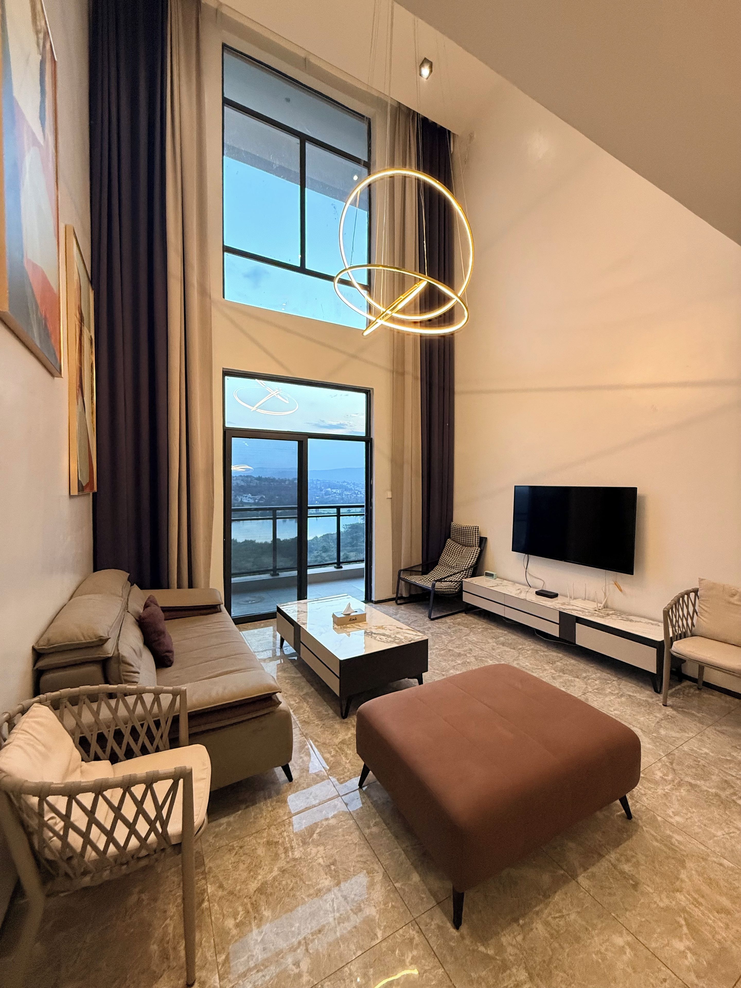 A modern living room with a sofa, ottoman, and a flat-screen TV.