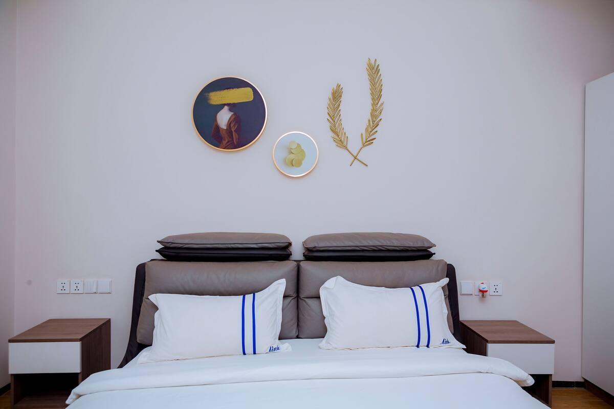 A neatly arranged bedroom with a bed, two nightstands, a wall-mounted artwork, and a decorative plant.